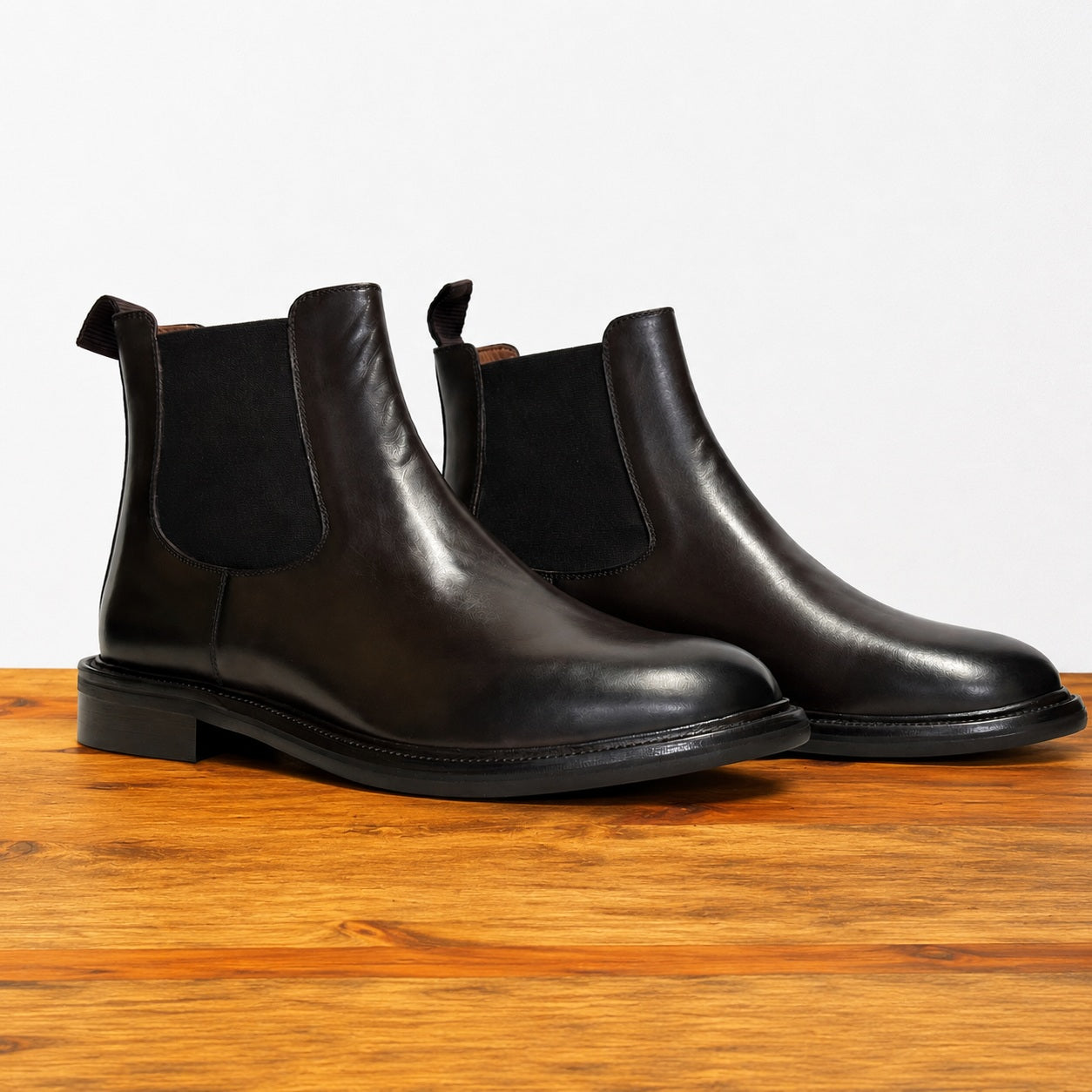 Pair of tobacco color leather Chelsea boots on a wooden surface with a light gray background