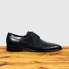 Black leather dress shoe on a wooden surface with a light gray background