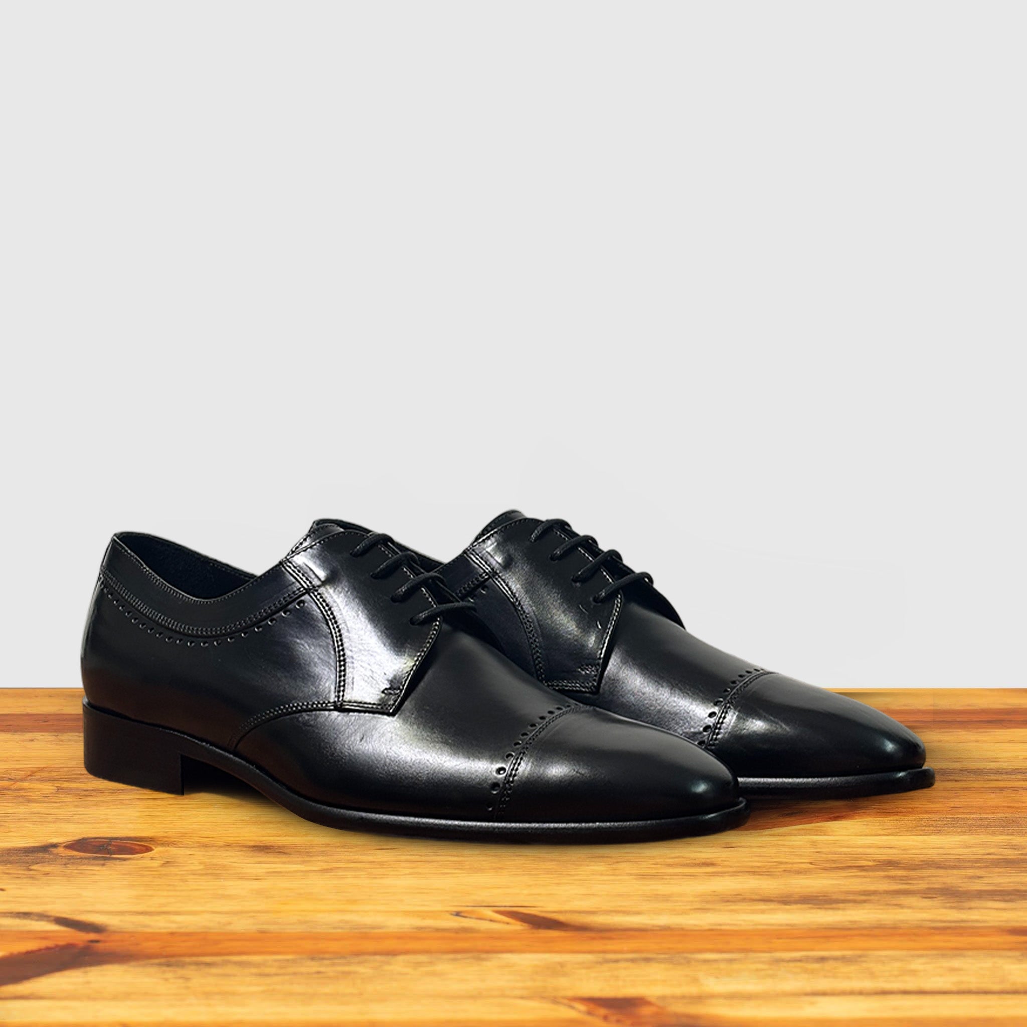 A pair of Black leather dress shoe on a wooden surface with a light gray background