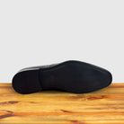 Outsole of Black leather dress shoe on a wooden surface with a light gray background