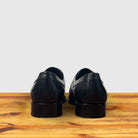Black leather dress shoe on a wooden surface with a light gray background