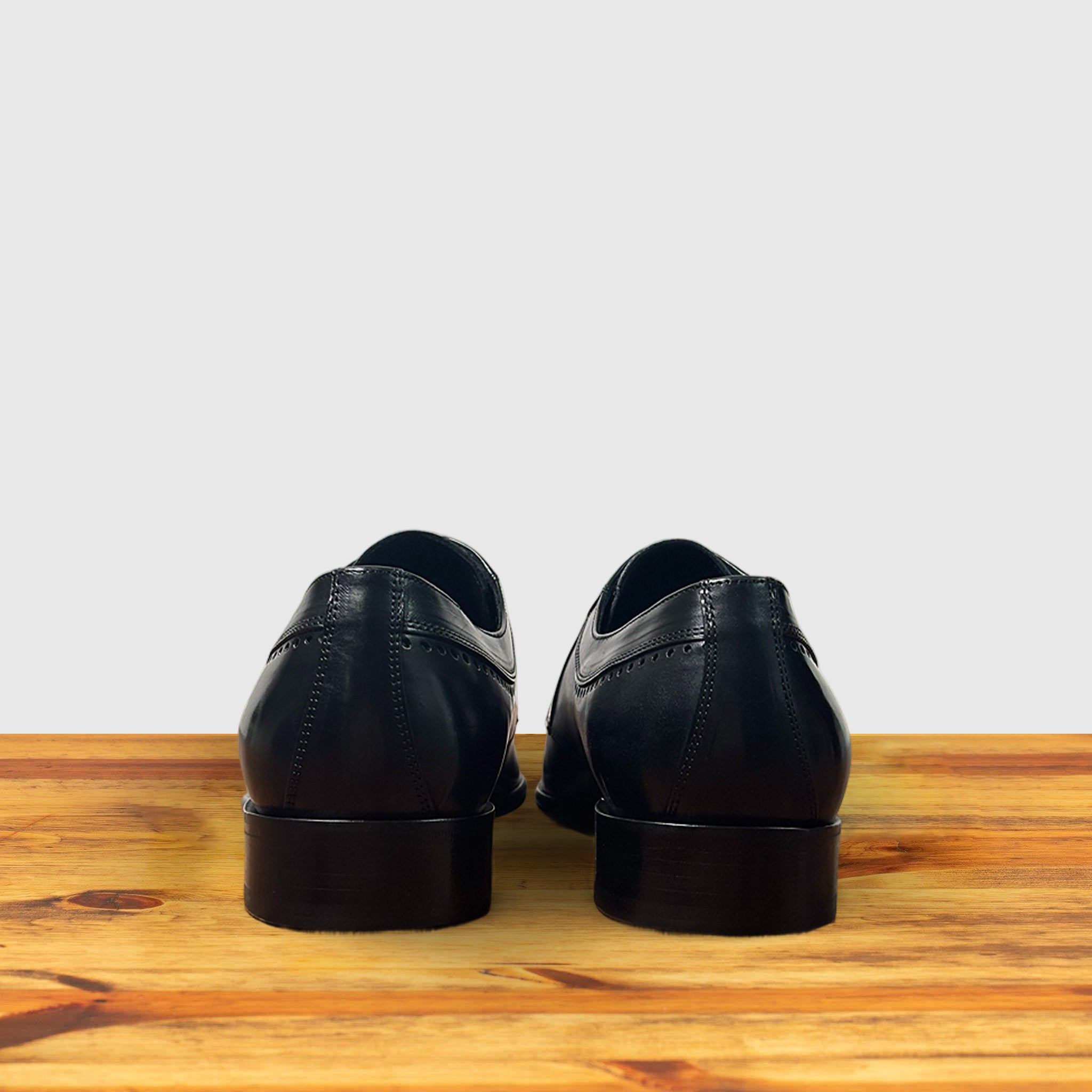 Black leather dress shoe on a wooden surface with a light gray background