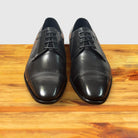 A pair of Black leather dress shoe on a wooden surface with a light gray background