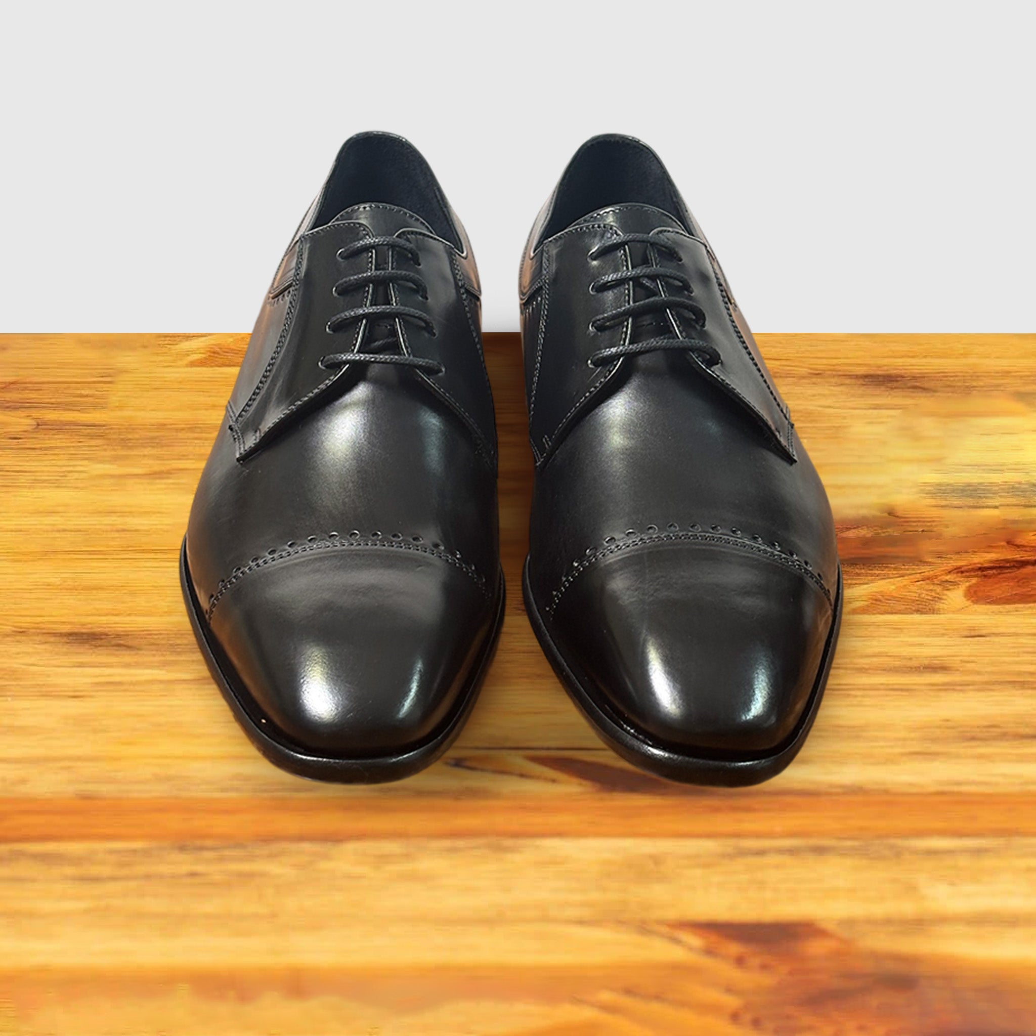 A pair of Black leather dress shoe on a wooden surface with a light gray background