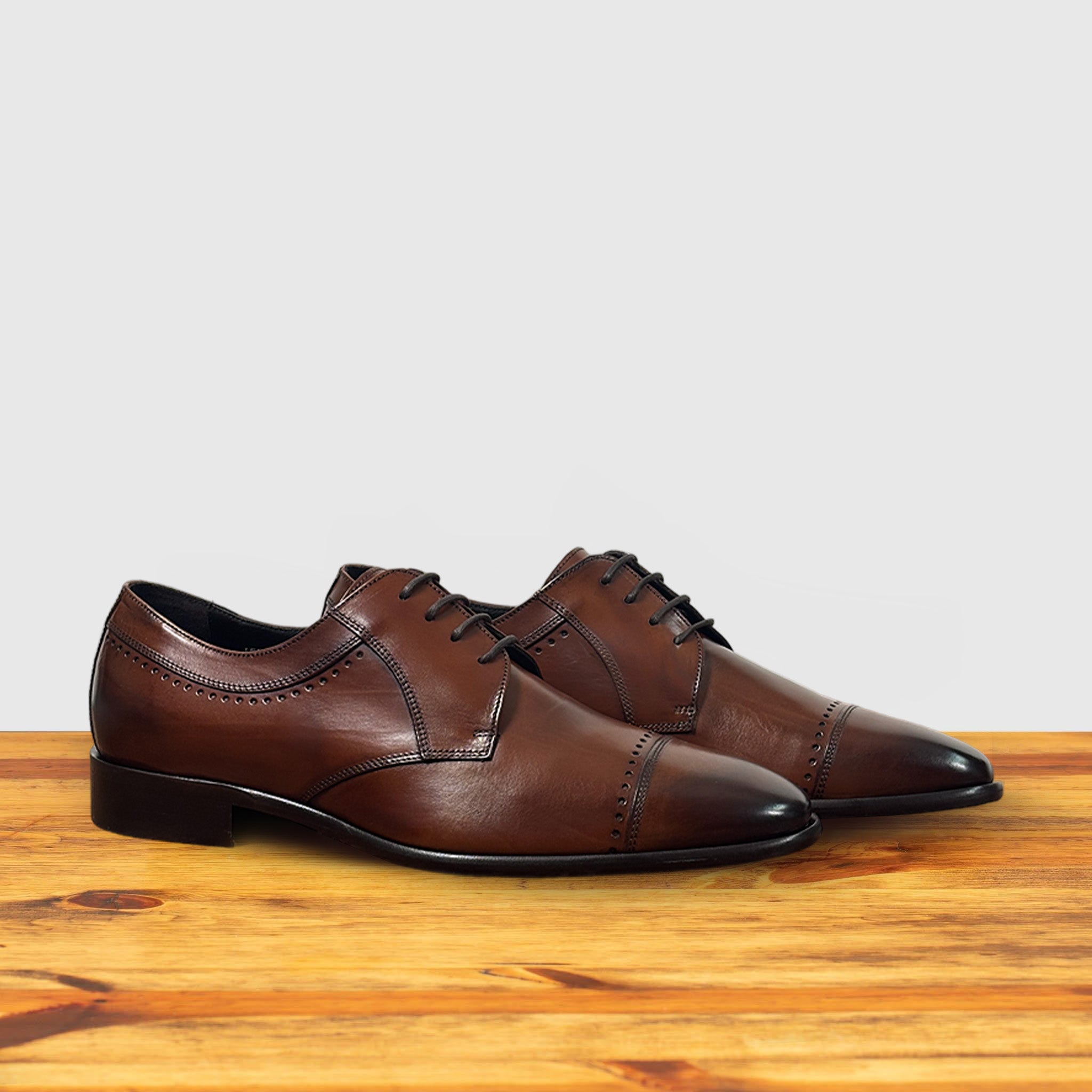 Pair of Brown leather dress shoe on a wooden surface with a light gray background