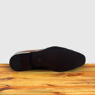 Outsole of Brown leather dress shoe on a wooden surface with a light gray background