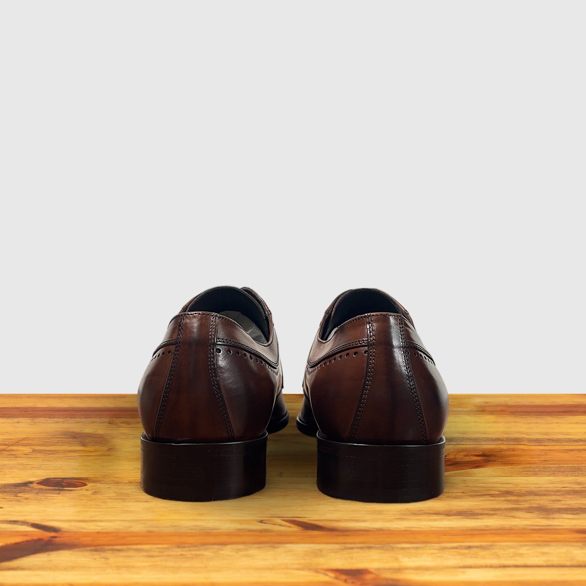A pair of Brown leather dress shoe on a wooden surface with a light gray background