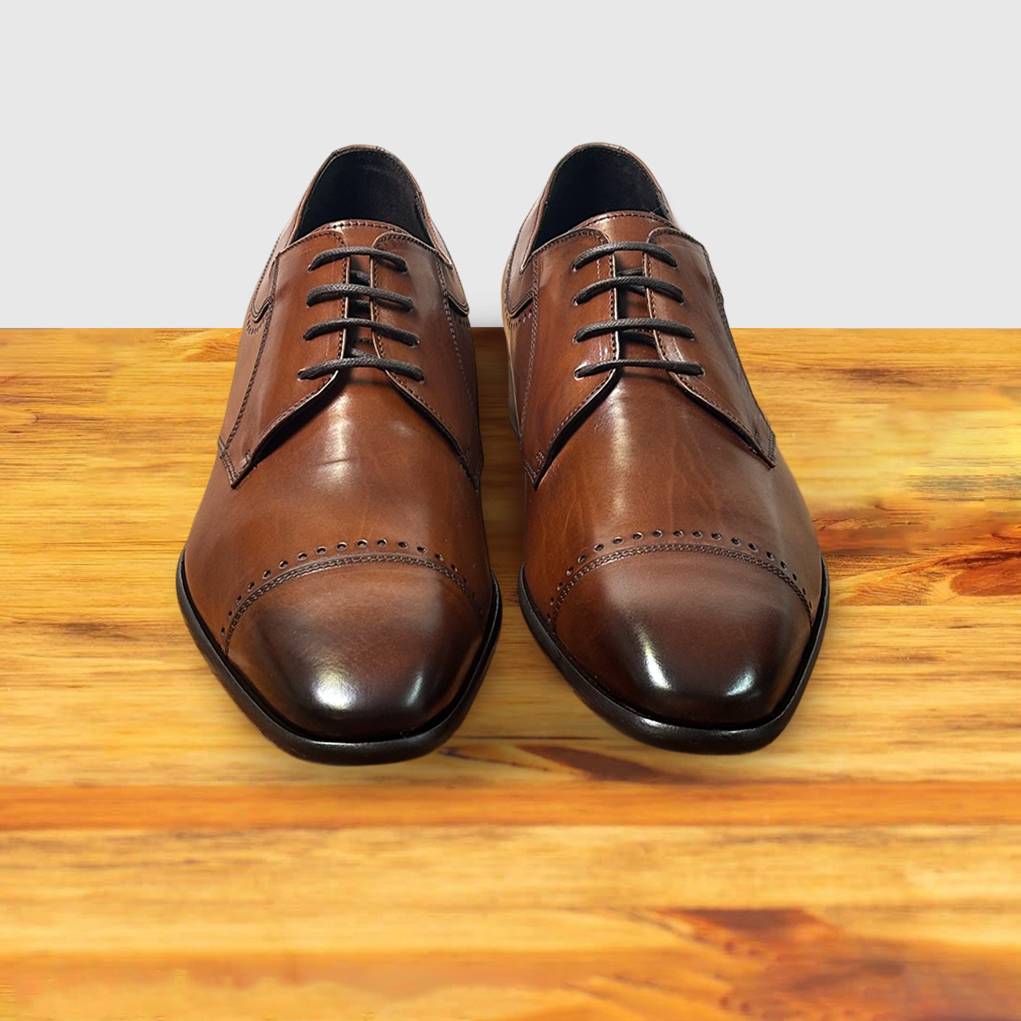 Brown leather dress shoe on a wooden surface with a light gray background