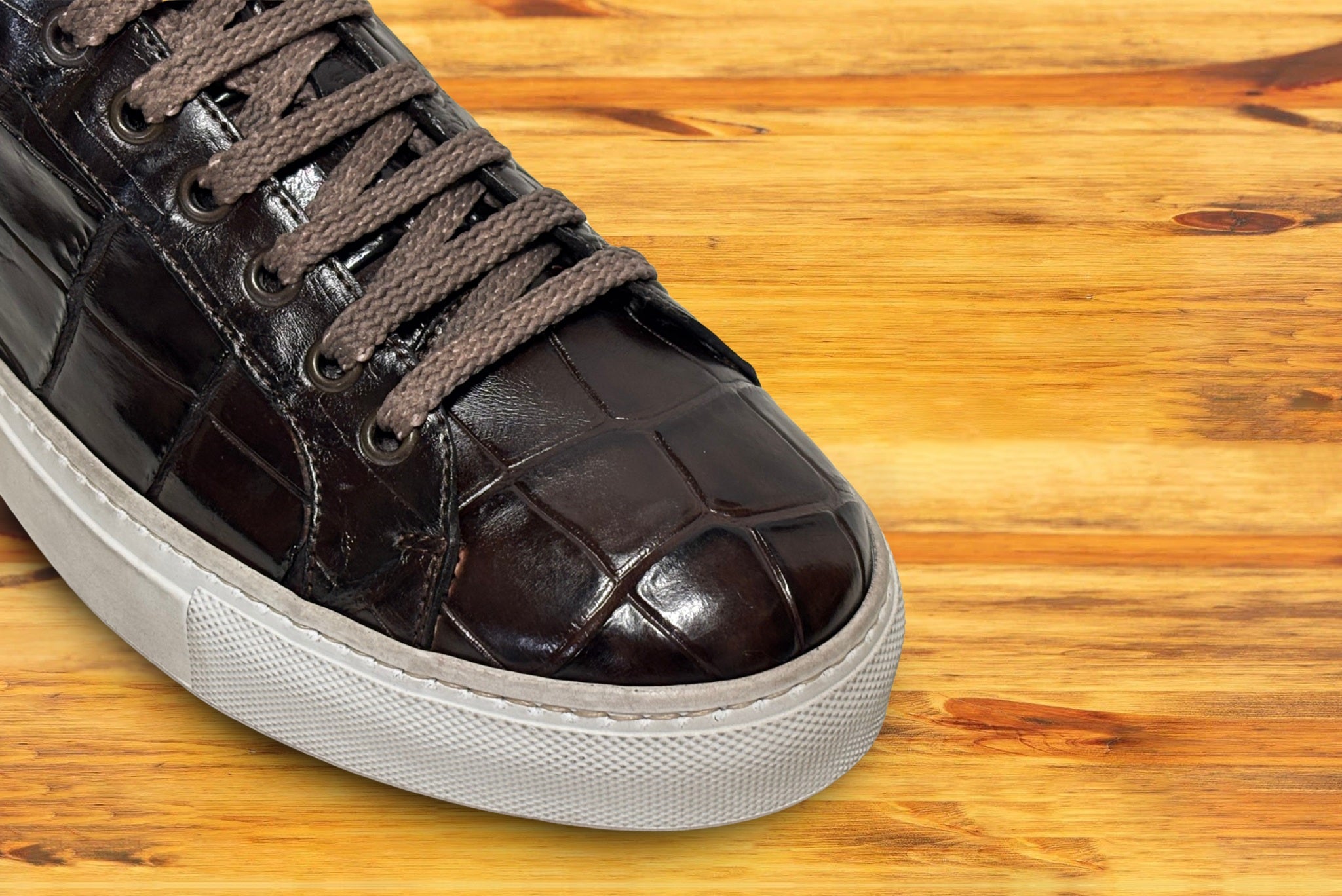 Brown leather sneaker with white sole on a wooden floor