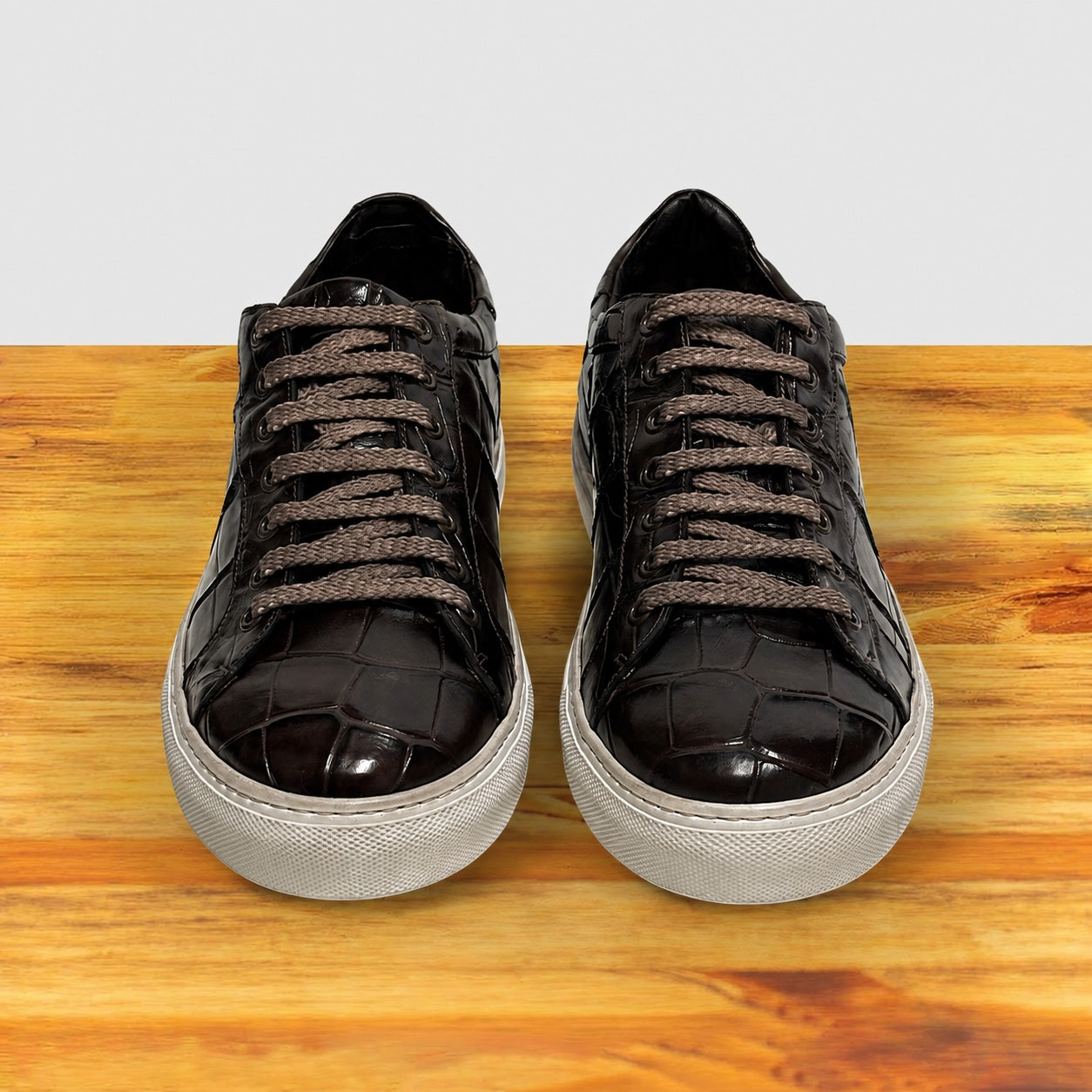 Pair of Dark Brown sneakers with white soles on a wooden surface