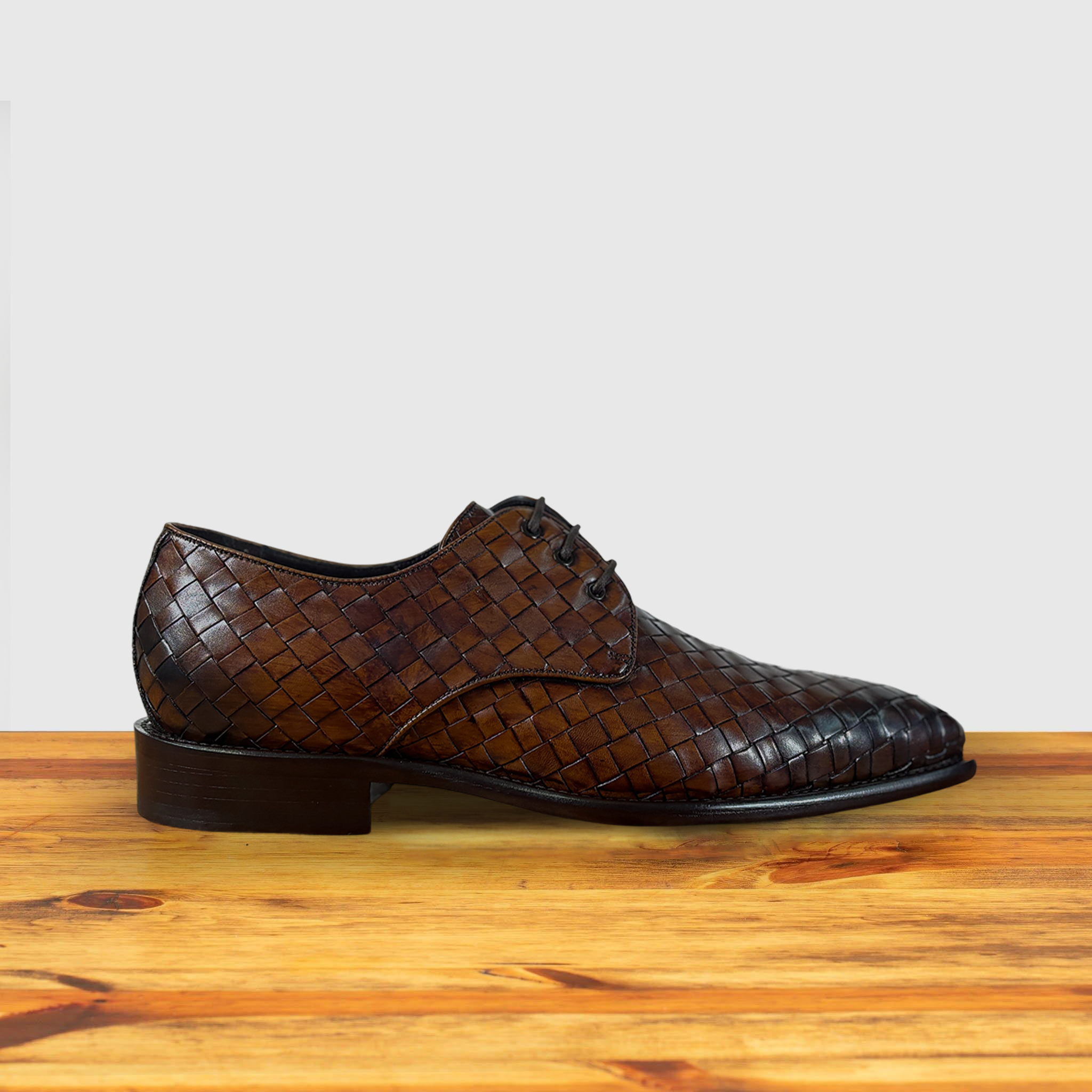 Brown woven leather shoe on a wooden surface with a light gray background