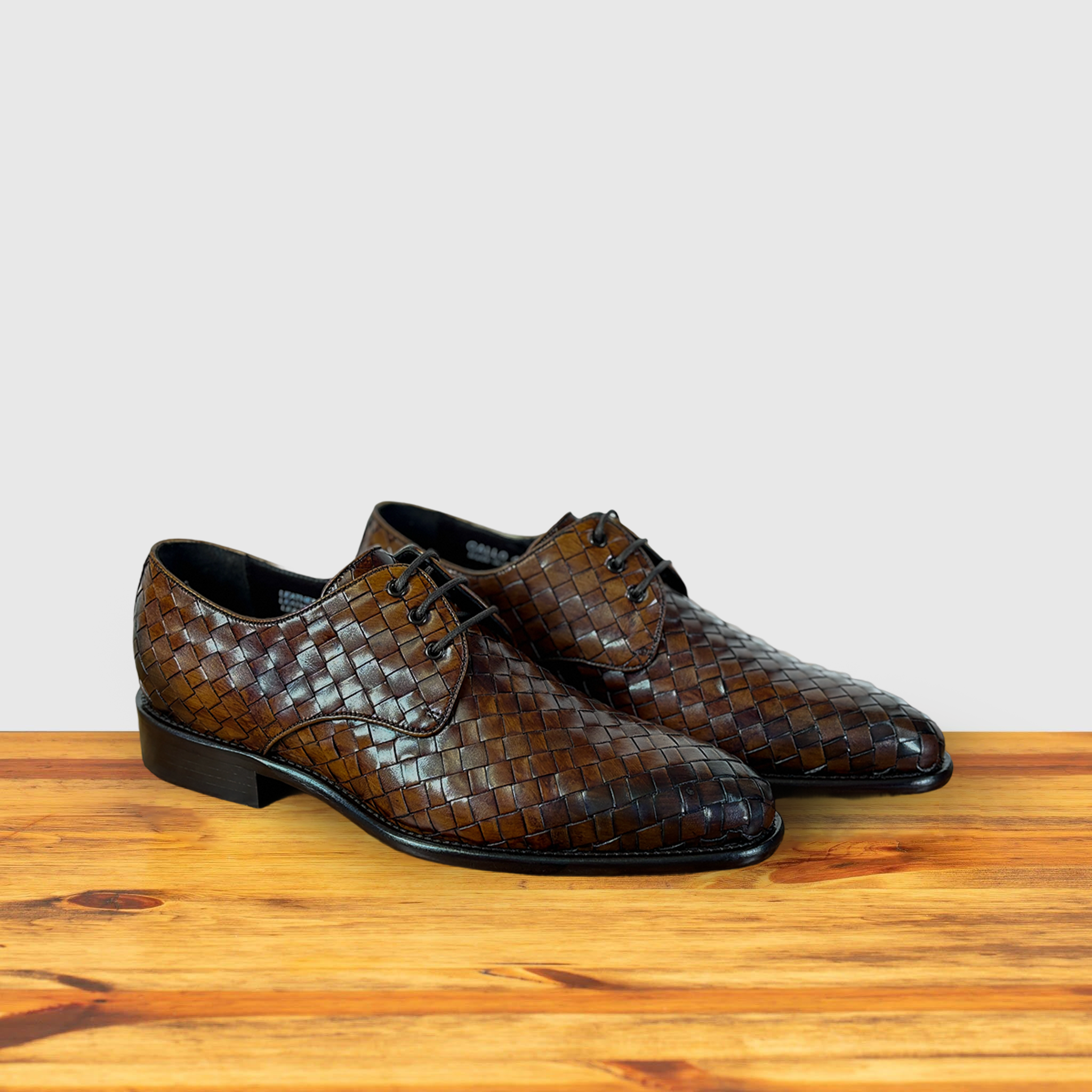 Pair of Brown woven leather shoe on a wooden surface with a light gray background
