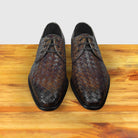 Pair of brown woven leather shoes on a wooden surface with a light gray background