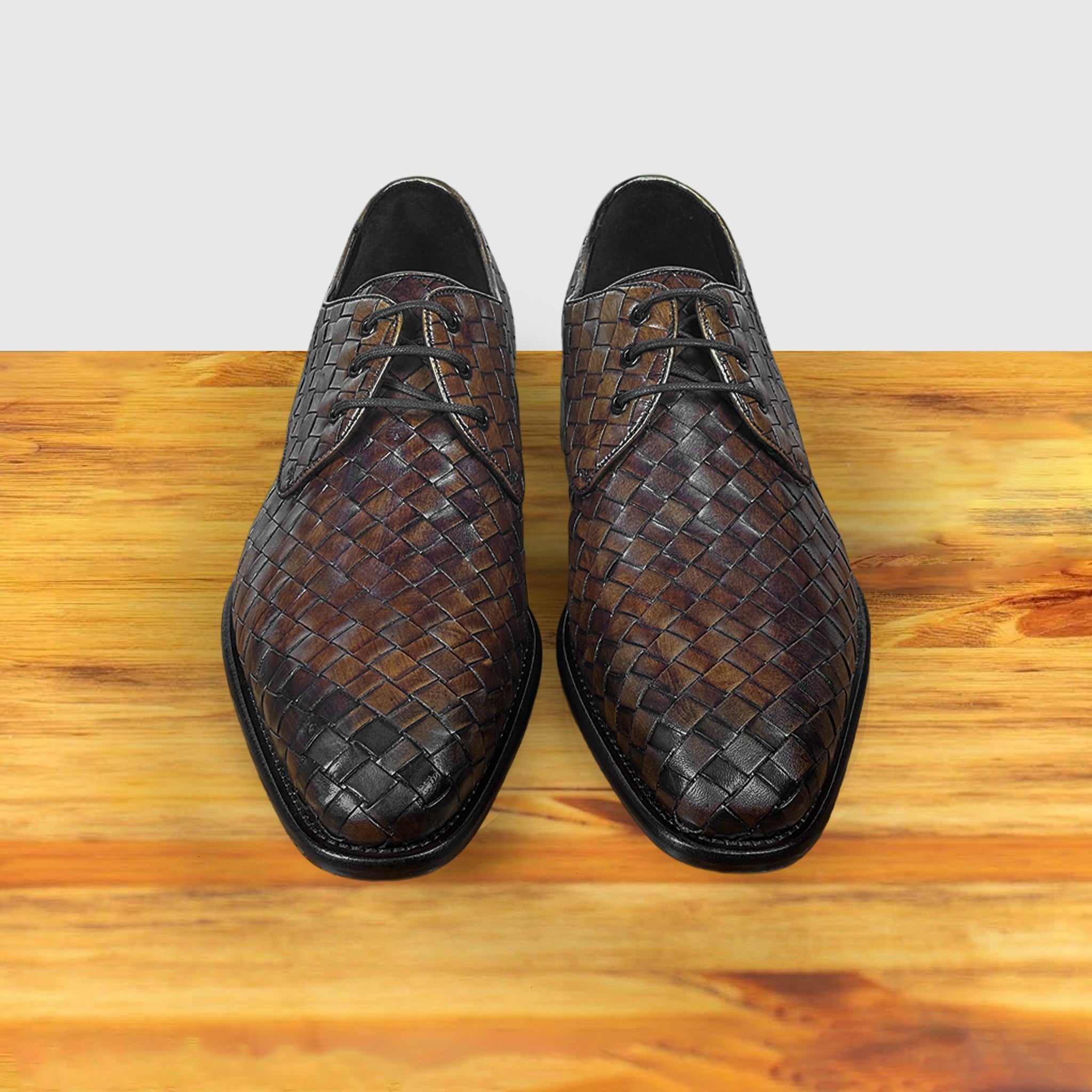 Pair of brown woven leather shoes on a wooden surface with a light gray background