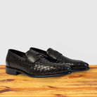 A pair of Brown woven loafer shoe on a wooden surface with a light gray background