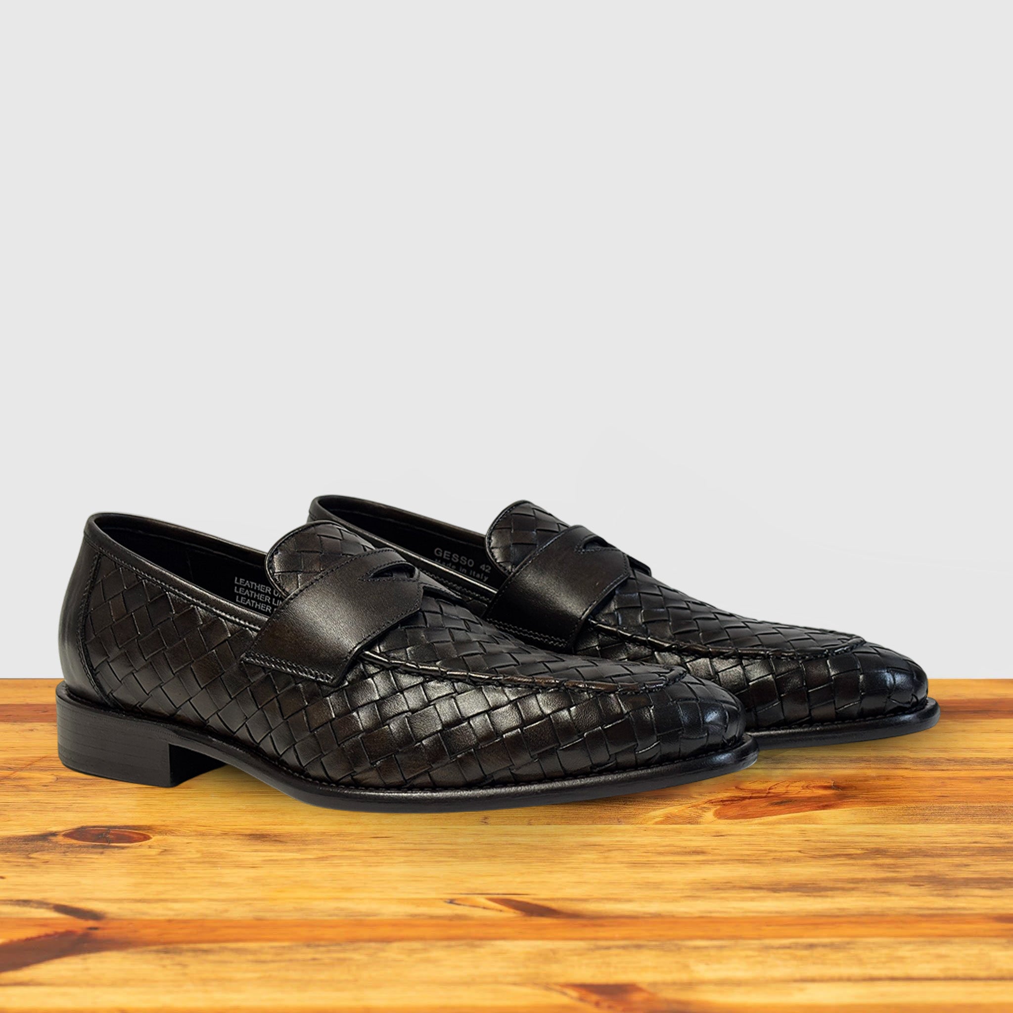 A pair of Brown woven loafer shoe on a wooden surface with a light gray background