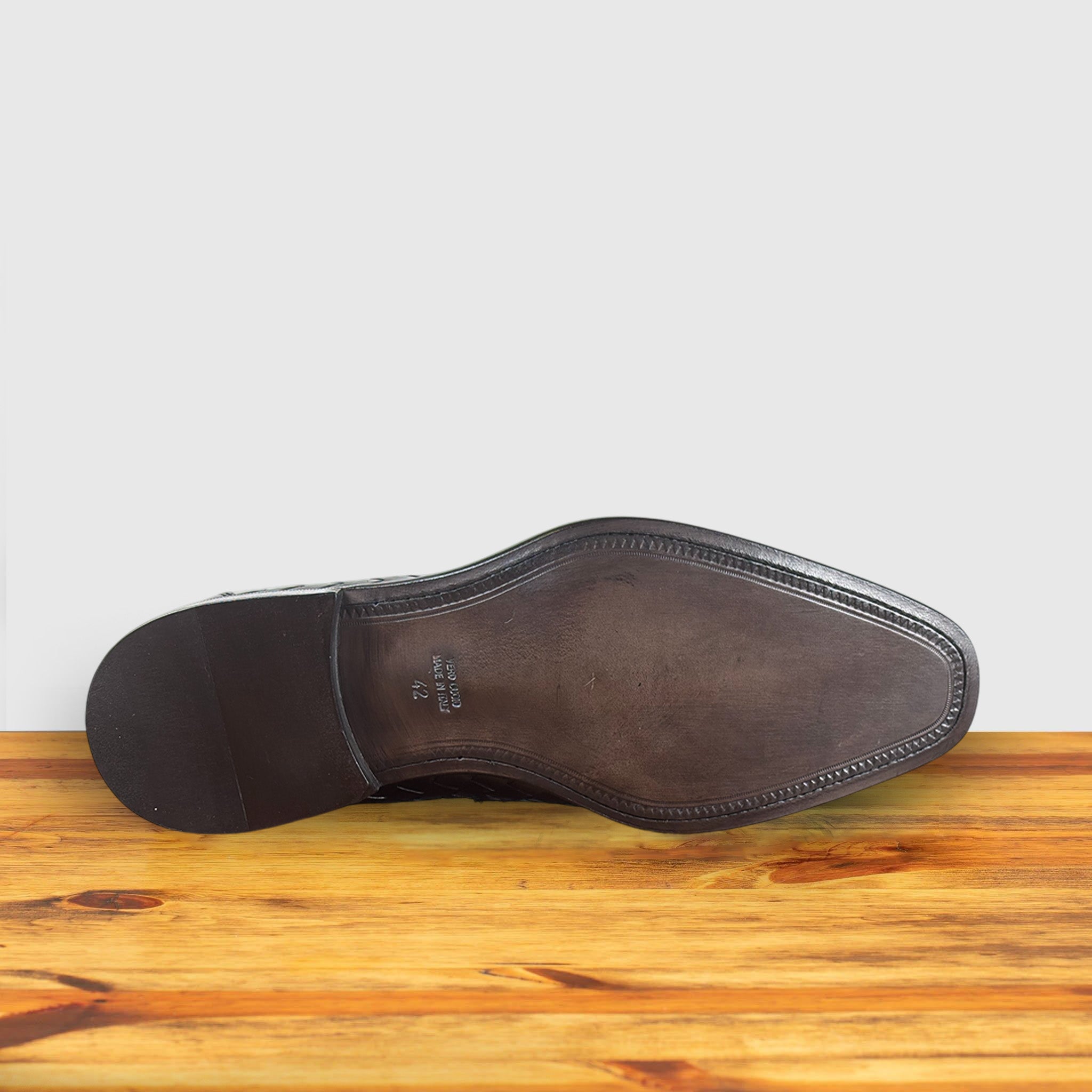 Outsole of Brown woven loafer shoe on a wooden surface with a light gray background