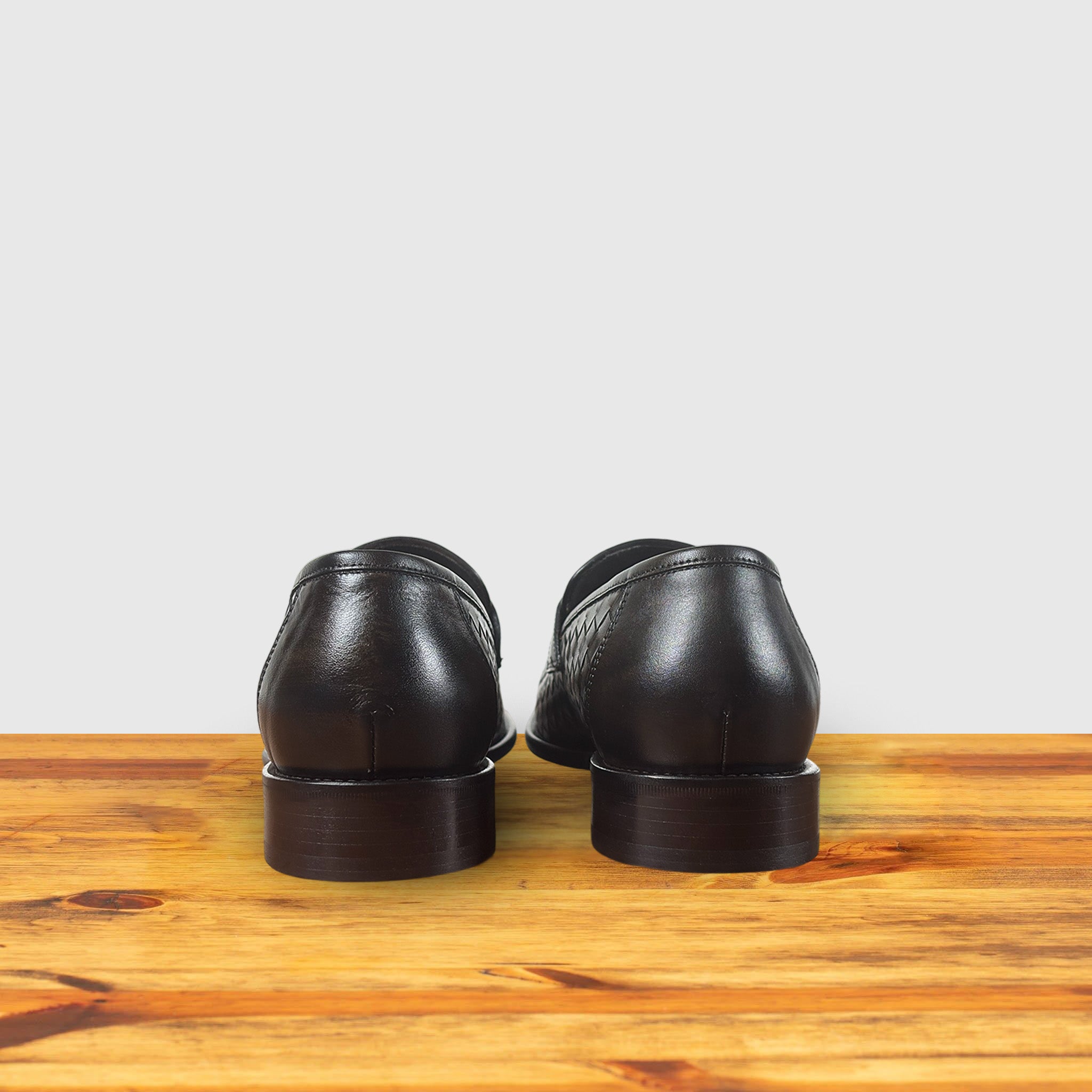 A pair of Brown woven loafer shoe on a wooden surface with a light gray background