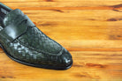 Green woven loafer shoe on a wooden surface