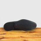 Outsole of Green woven loafer shoe on a wooden surface with a light gray background