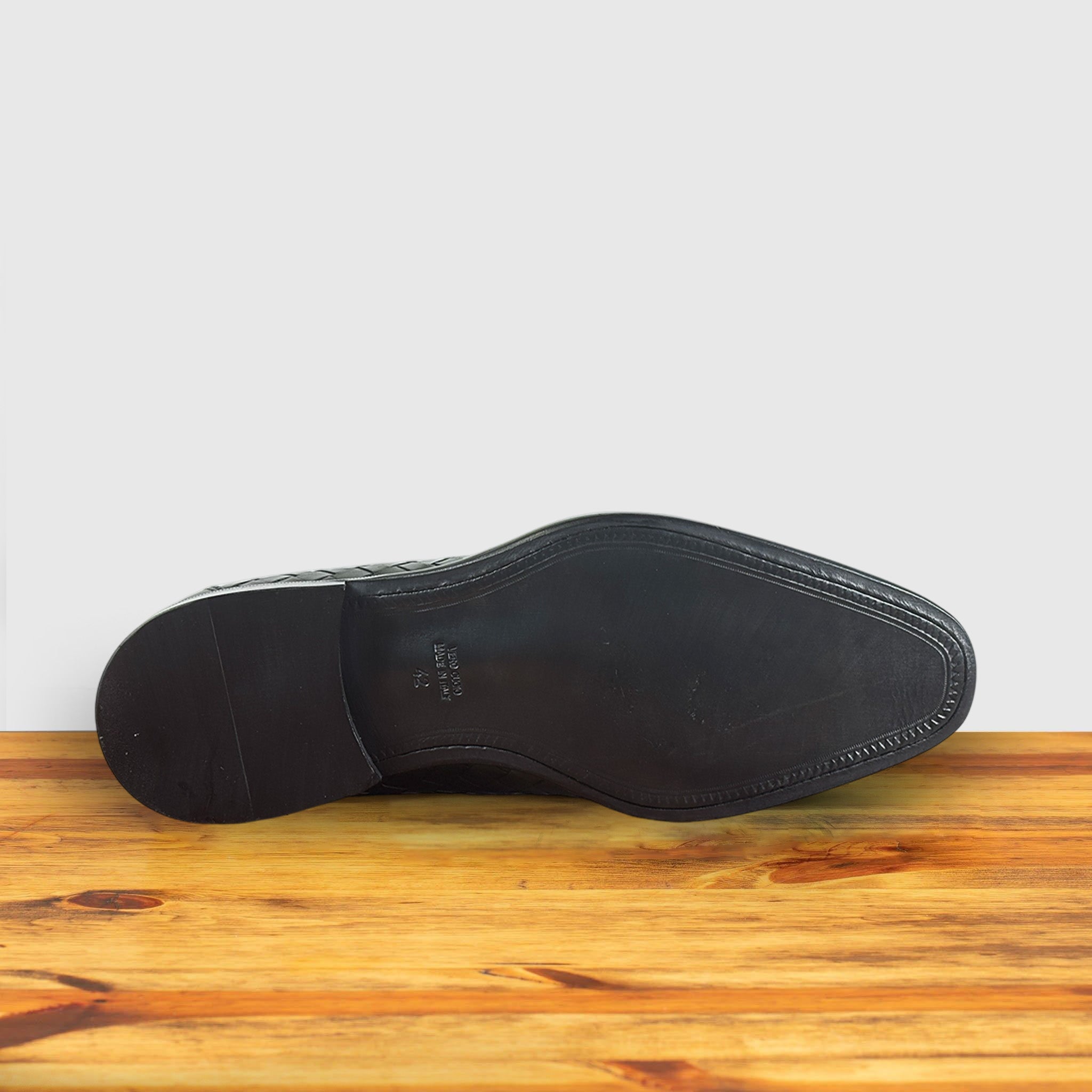 Outsole of Green woven loafer shoe on a wooden surface with a light gray background