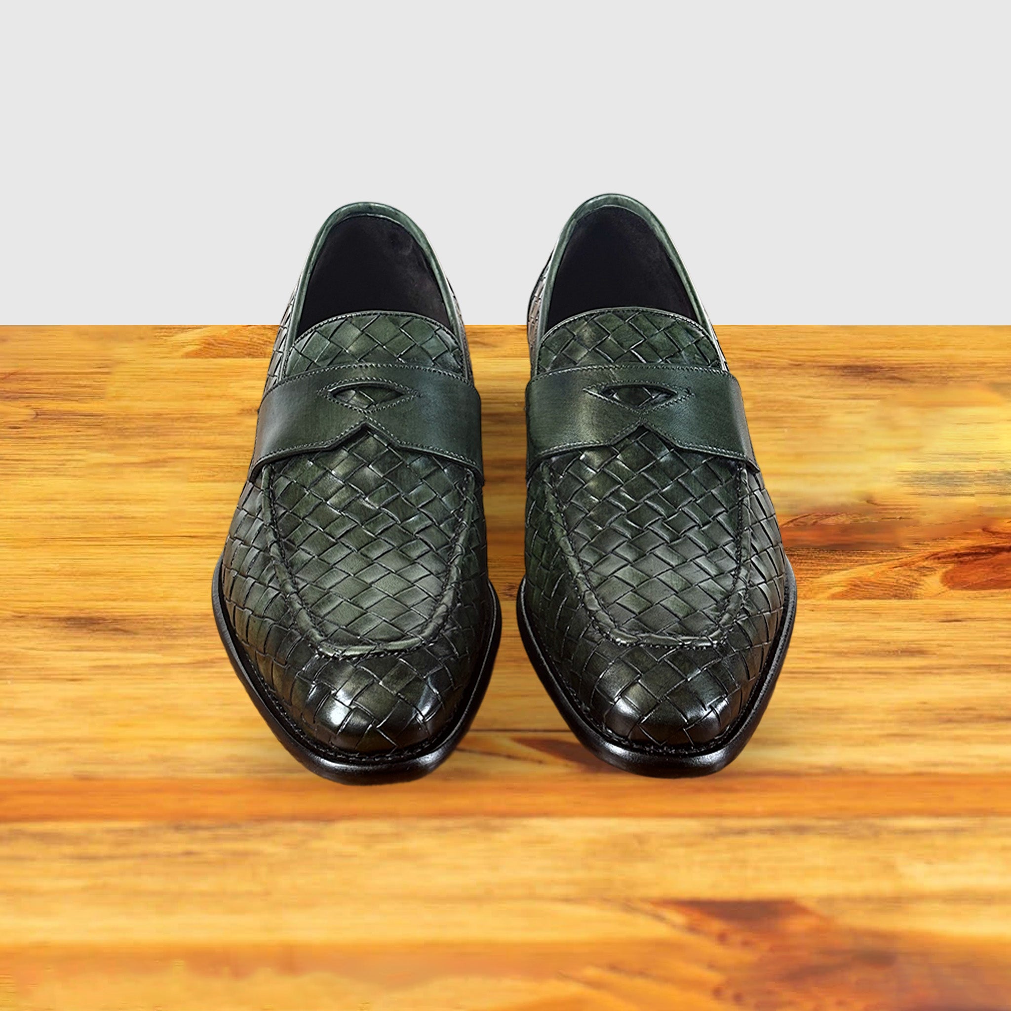 A pair of Green woven loafer shoe on a wooden surface with a light gray background