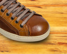 Brown leather sneaker with gray laces on a wooden surface