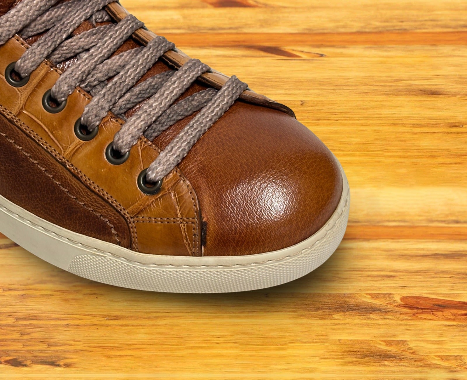 Brown leather sneaker with gray laces on a wooden surface