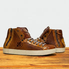 Brown leather high-top sneakers with zippers on a wooden surface and light gray background