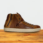 Brown high-top sneaker with a logo on a wooden surface