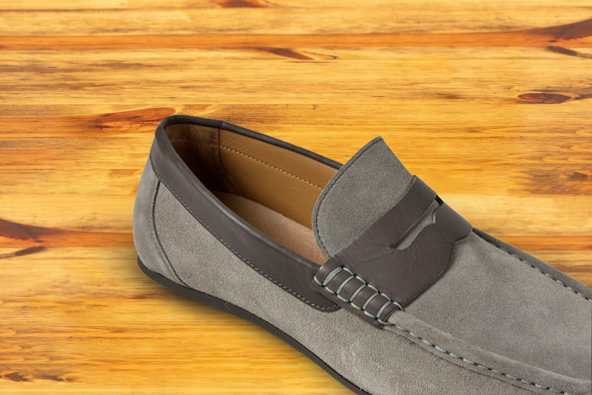 A suede penny loafer with a strap, in a gray color, displayed on a wooden surface.