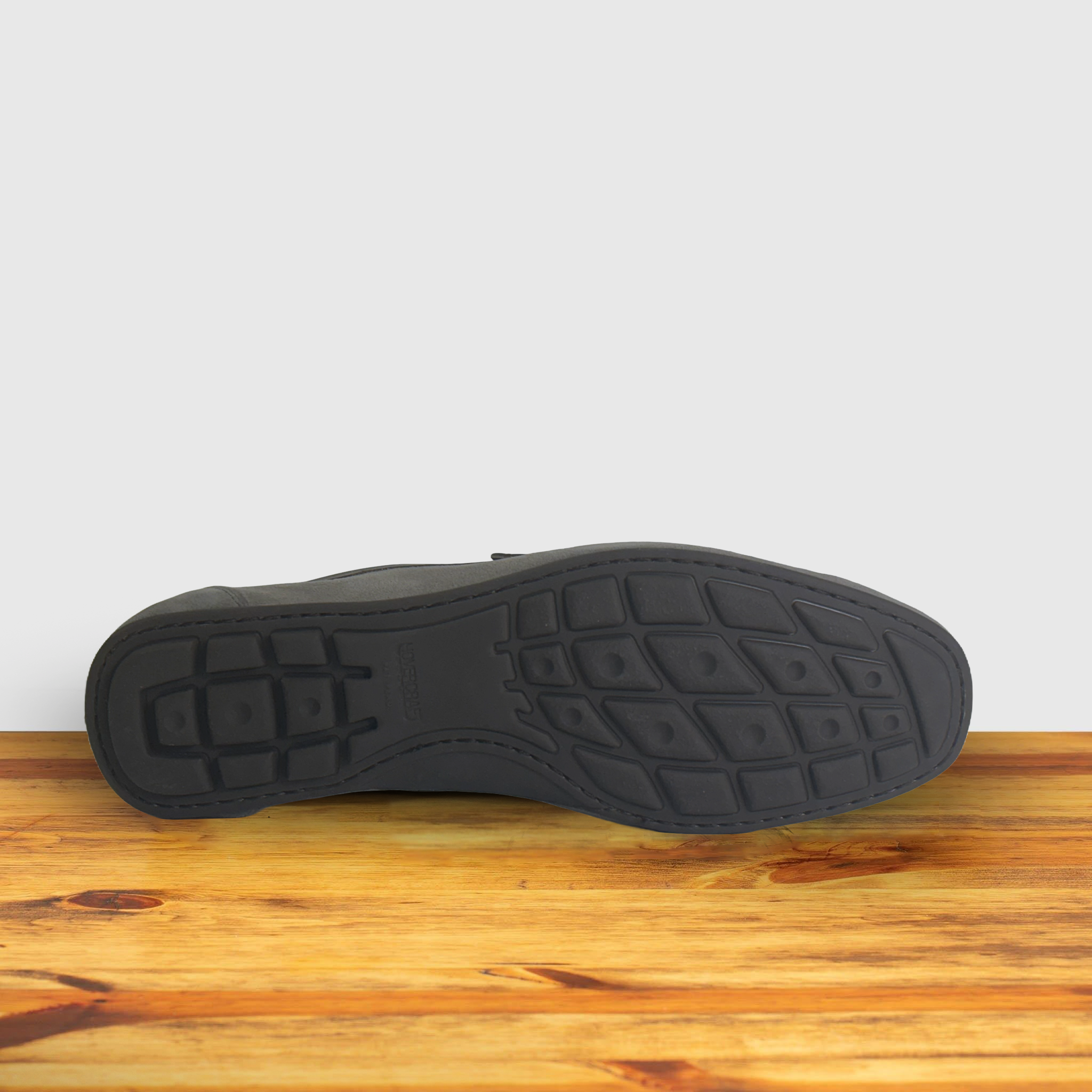 Outsole of  suede penny loafer with a strap, in a gray color, displayed on a wooden surface.