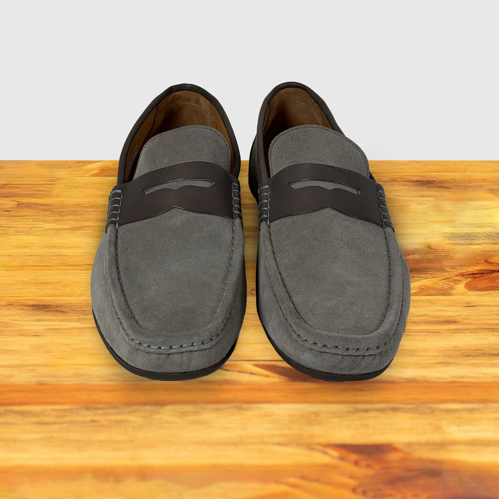 A Pair of  suede penny loafer with a strap, in a gray color, displayed on a wooden surface.