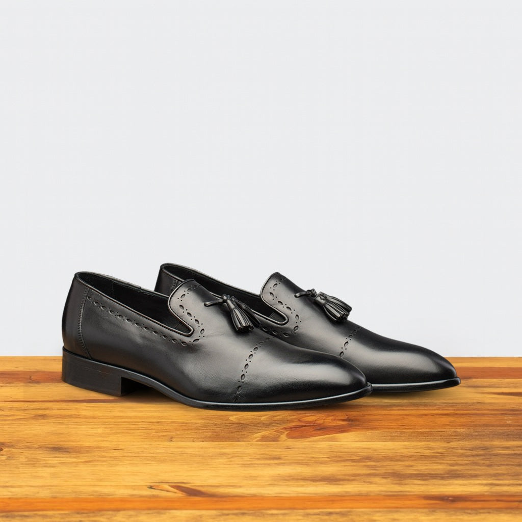 Pair of black leather loafers on a wooden surface with a light gray background