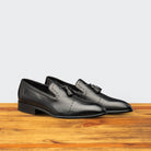 Pair of black leather loafers on a wooden surface with a light gray background