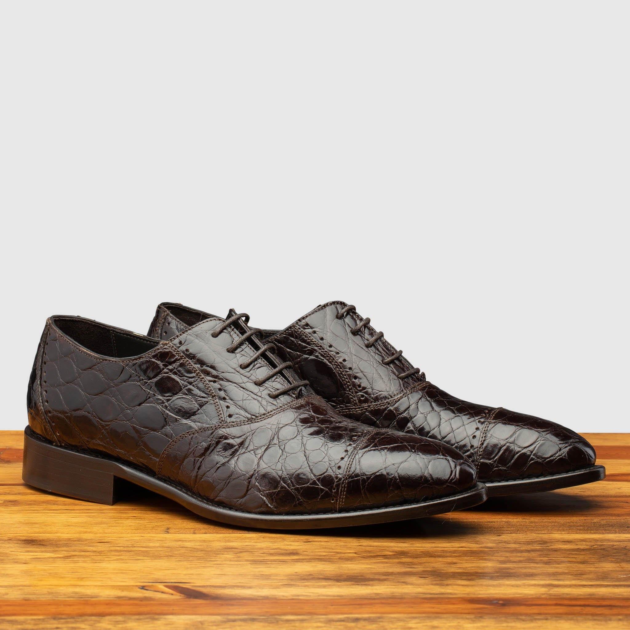 Pair of brown alligator  leather dress shoes on a wooden surface with a light gray background