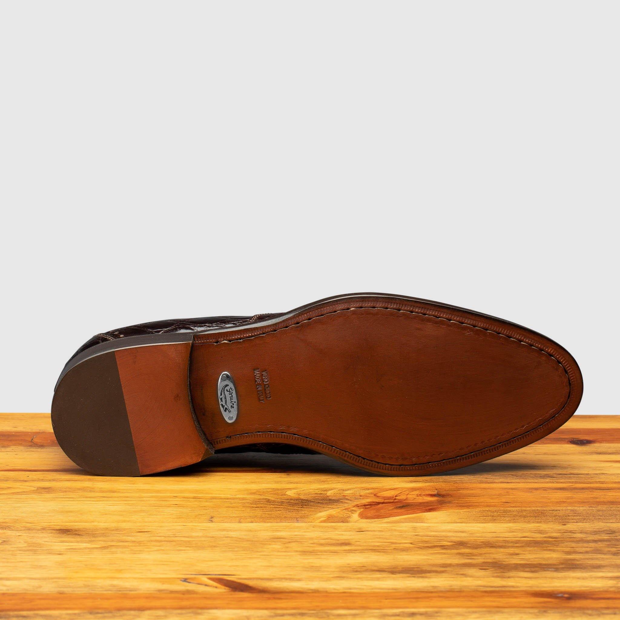 Outsole of brown alligator leather dress shoes on a wooden surface with a light gray background