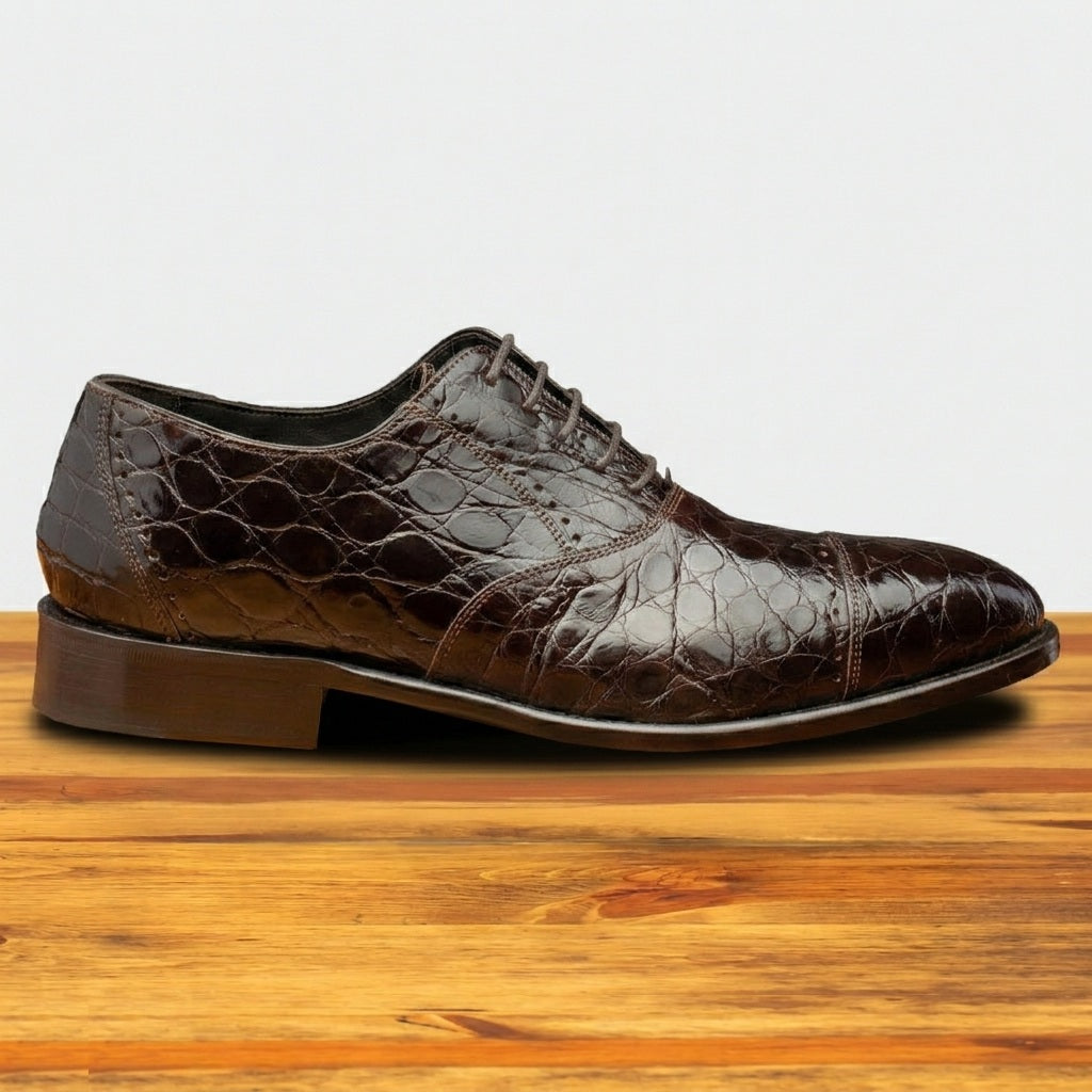 Brown leather shoe with crocodile texture on a wooden surface