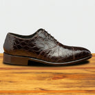Brown leather shoe with crocodile texture on a wooden surface
