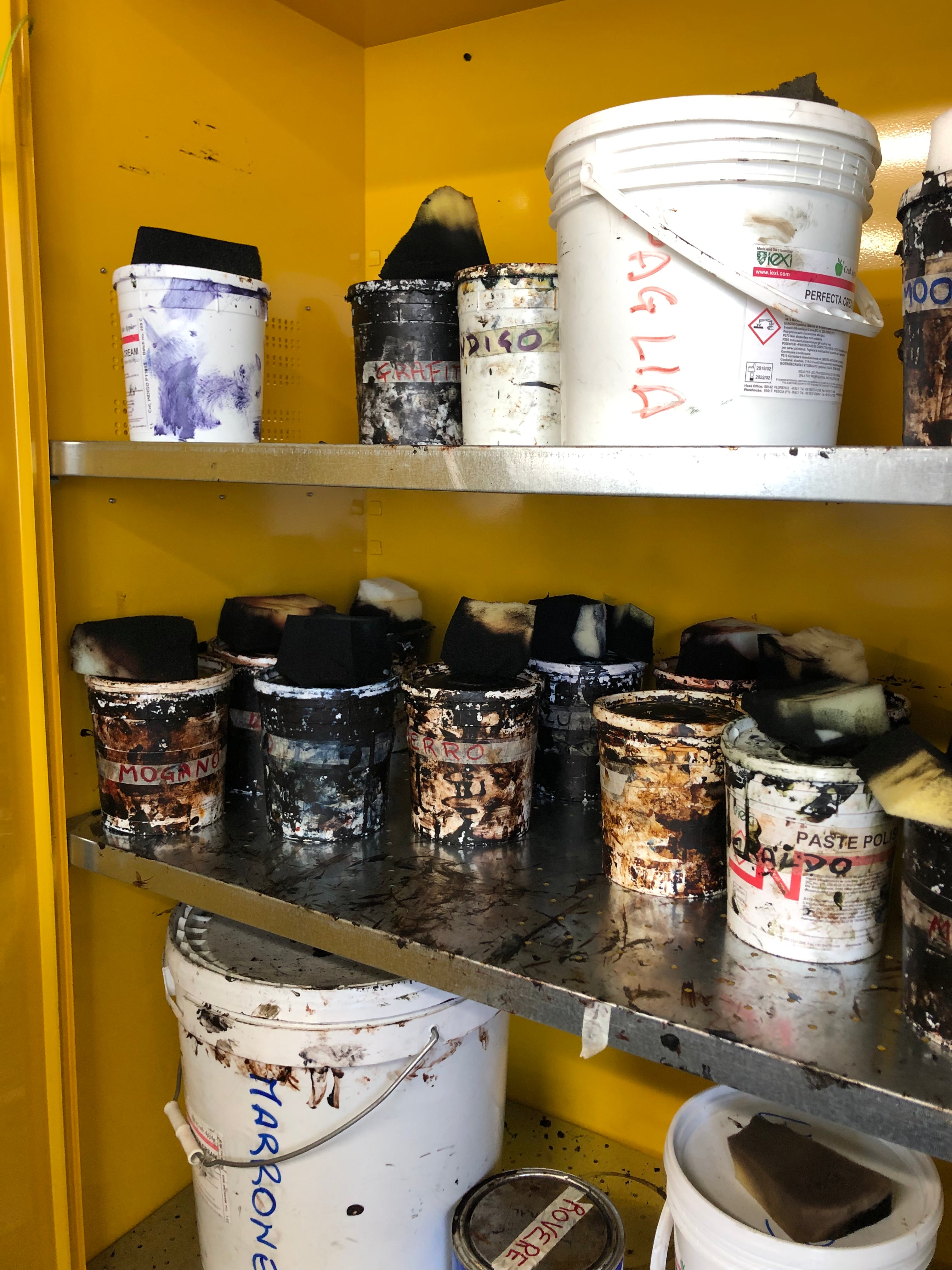 Shelves of Italian leather edge dye and finishing paste pots labelled by colour at the Calzoleria Toscana shoe factory — used for hand-finishing men's dress shoes