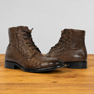 A pair of brown textured leather lace-up ankle boots with a crocodile-embossed pattern, displayed on a wooden surface against a light gray background.