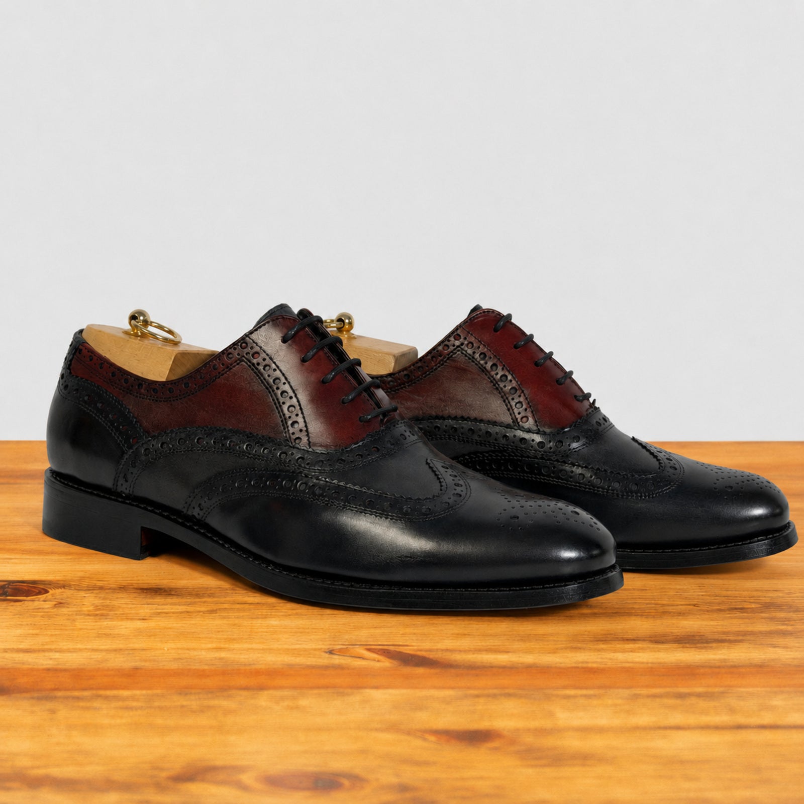 A pair of men's blue and Bordeaux  oxford shoes with black laces, displayed on a wooden surface against a light gray background.