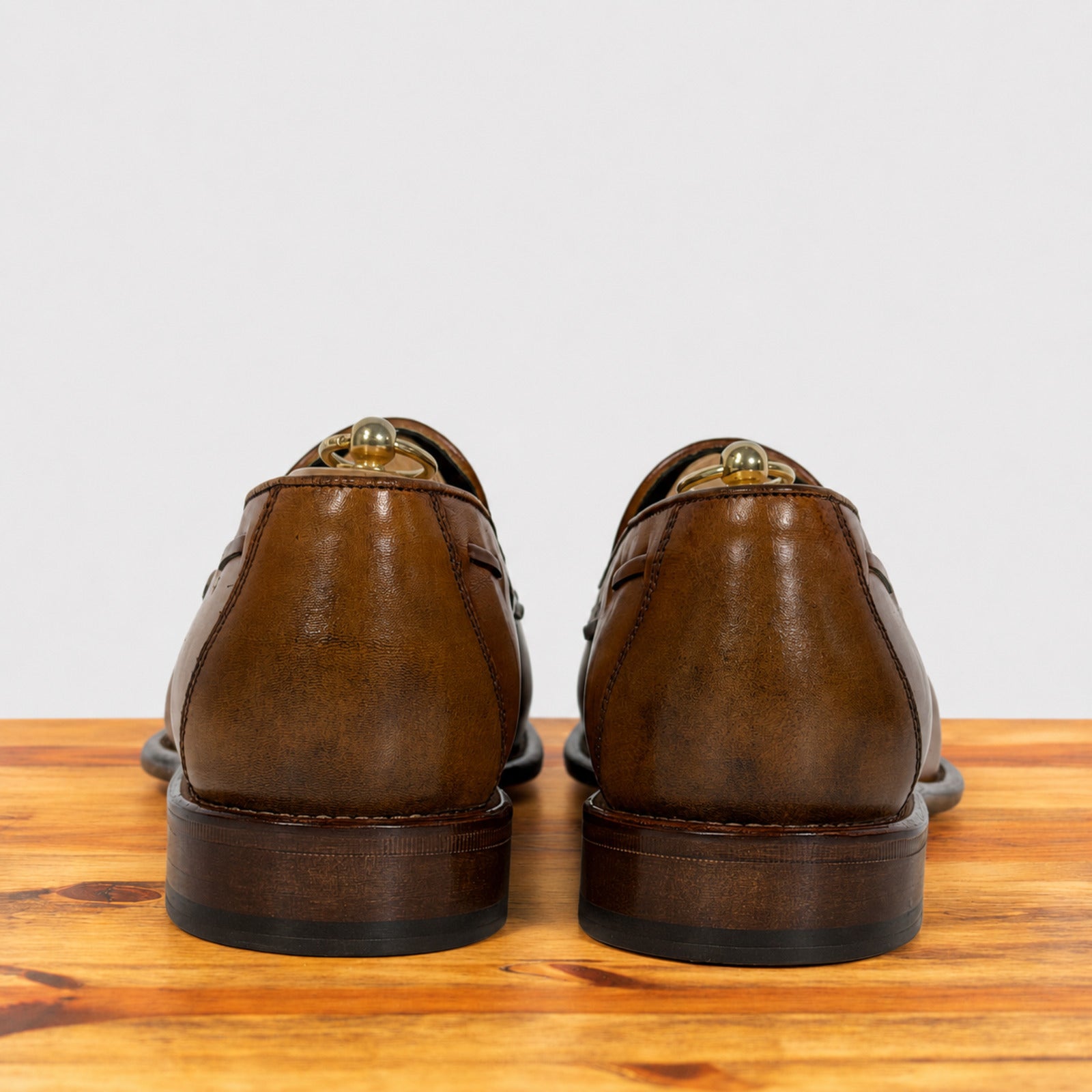A pair of Dark Caramel leather boat shoes shown from the back, resting on a wooden surface against a light gray background.