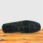 The outsole of a shoe with a green and black Genuine Crocodile loafer, resting on a wooden surface against a light gray background.