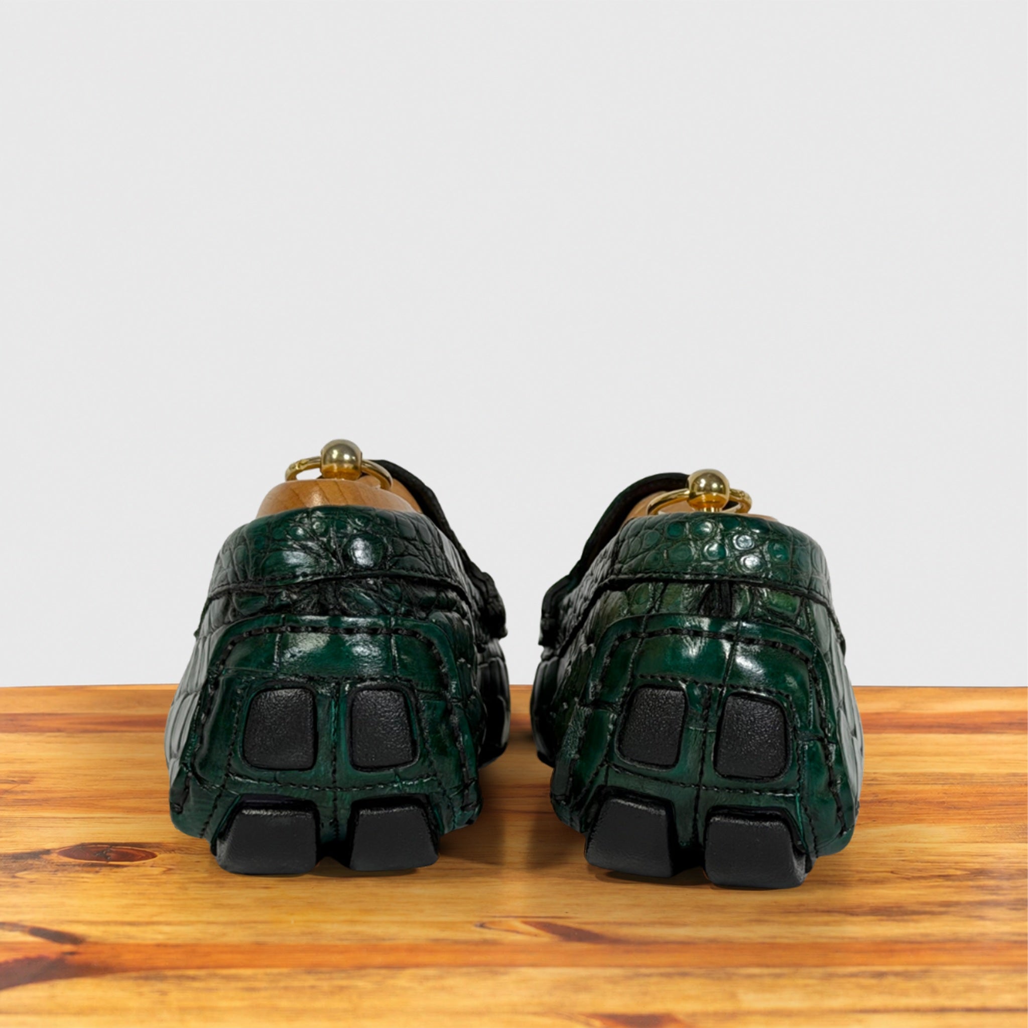 A pair of Emerald Green Genuine Crocodile leather shoes viewed from the back, resting on a wooden surface against a light gray background.