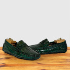 A pair of Emerald Green Genuine Crocodile leather loafers, displayed on wooden shoe trees on a light wood surface against a plain light gray background.