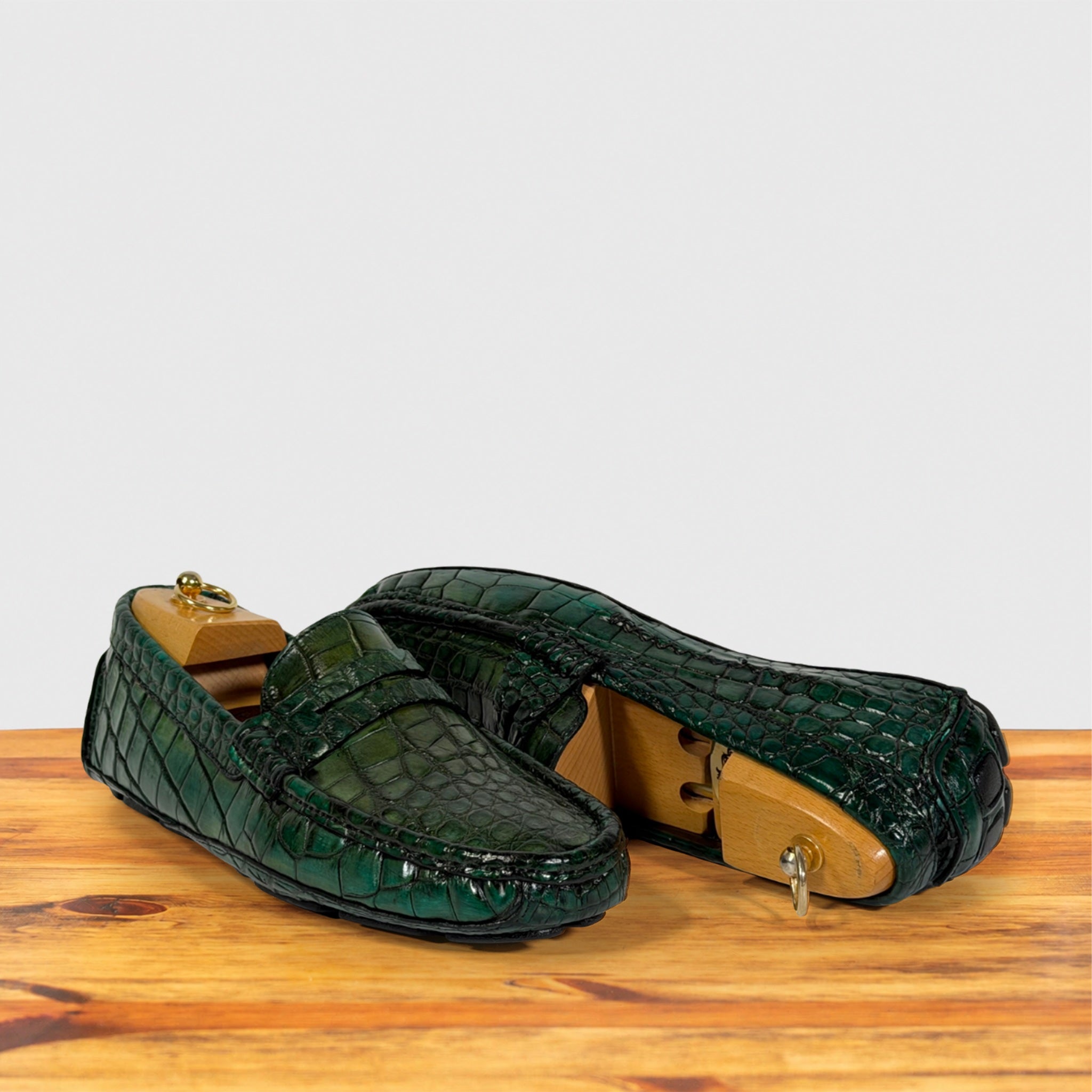 A pair of Emerald Green Genuine Crocodile leather loafers resting on a wooden surface against a light gray background.