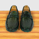 A pair of  Emerald Green Genuine Crocodile leather loafers displayed on wooden shoe stands over a light wood surface against a white background.