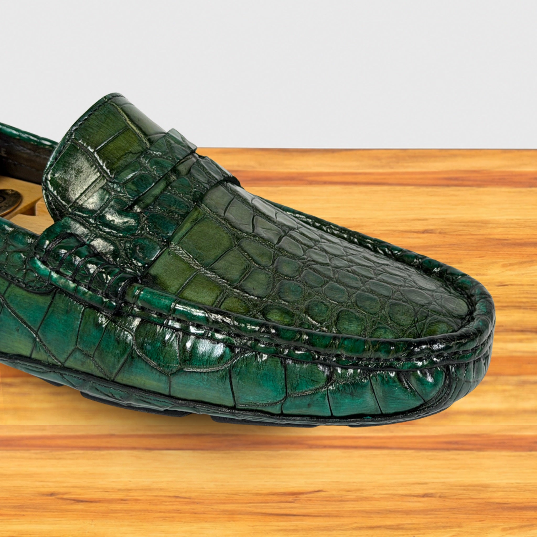 A single Emerald Green Genuine Crocodile loafer shoe resting on a light brown wooden surface against a white background.
