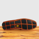 The outsole of a brown Genuine Crocodile leather shoe resting on a wooden surface against a light gray background.